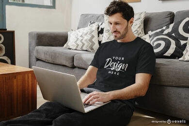 Maquete de camiseta preta homem na sala de estar com laptop