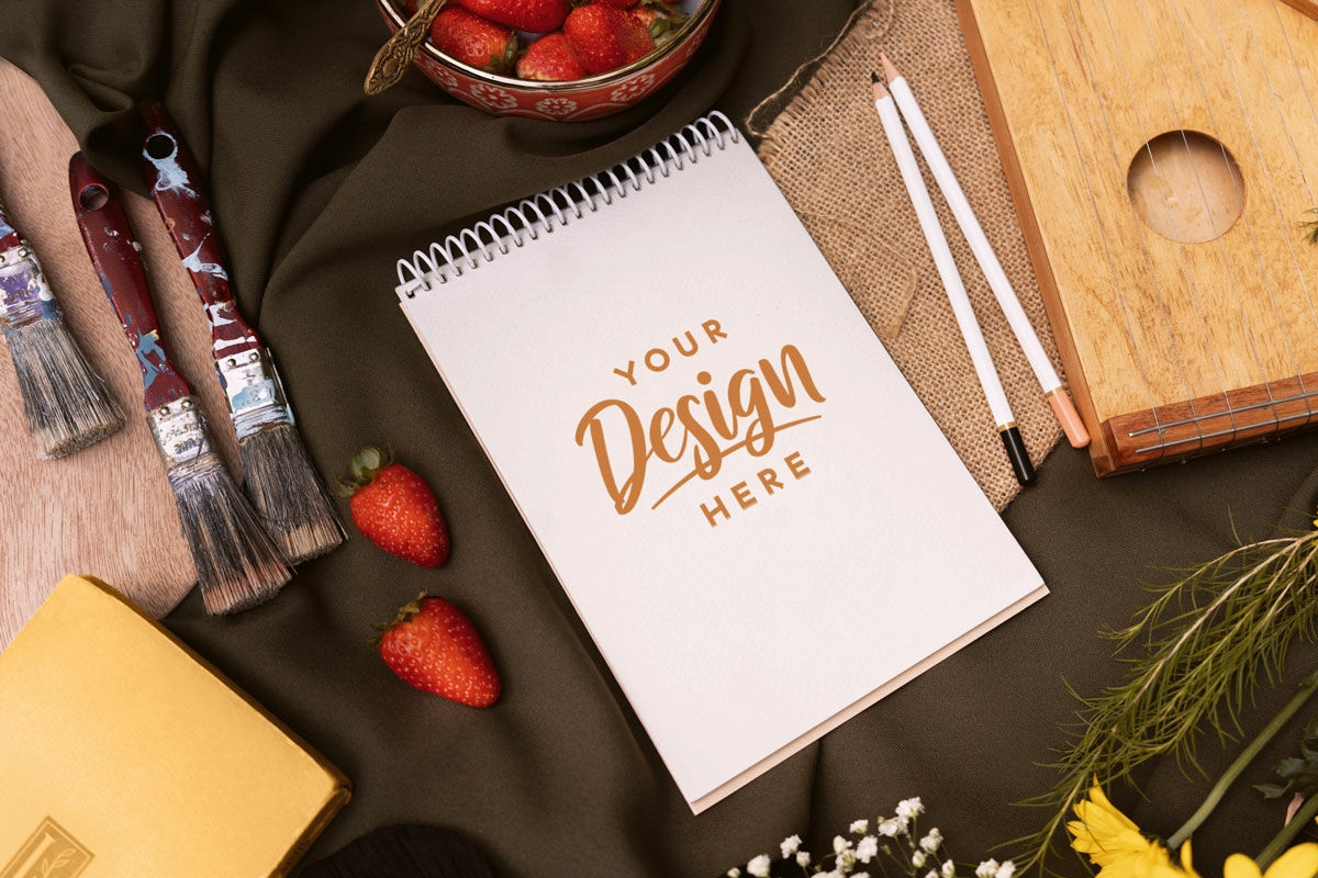 Notebook on table cloth with paint brushes mockup